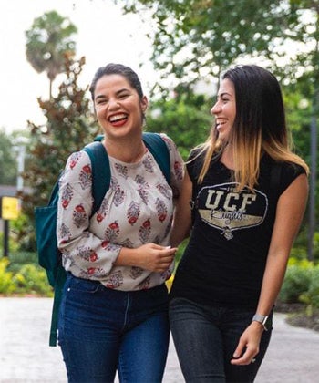 two female students with dark hair, walking outside while laughing