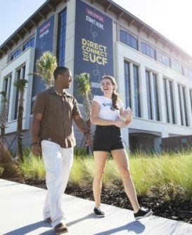 a male and female student walk by direct connect to ucf sign on campus building