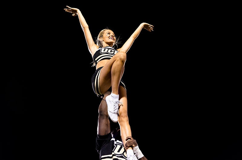 A 첥 cheerleader holds another cheerleader in the air.