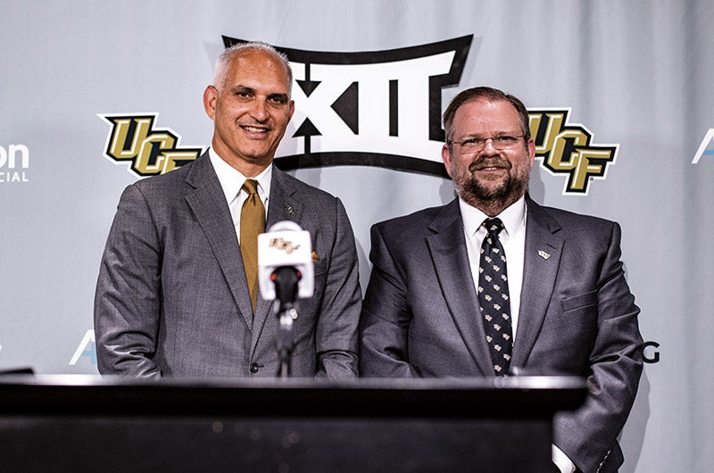 Two men in suits standing at a podium with a backdrop with 첥 and Big 12 logos behind them.